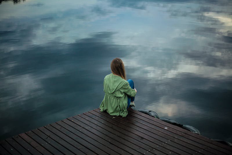 Woman sitting alone next to lake Femcel