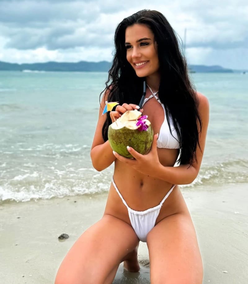 Adel in witte bikini op strand met kokosnoot