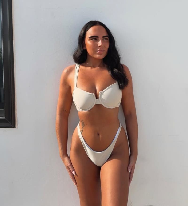 Sexy brunette in white bikini in front of white wall