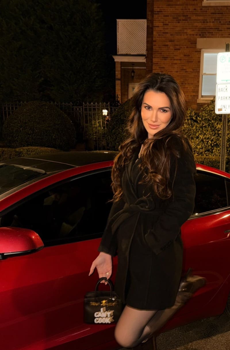 Andrea in zwarte jurk naast rode auto