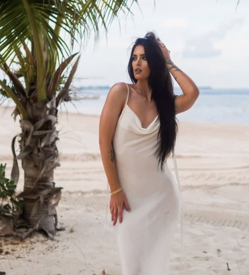 Hete brunette in witte lange jurk op strand